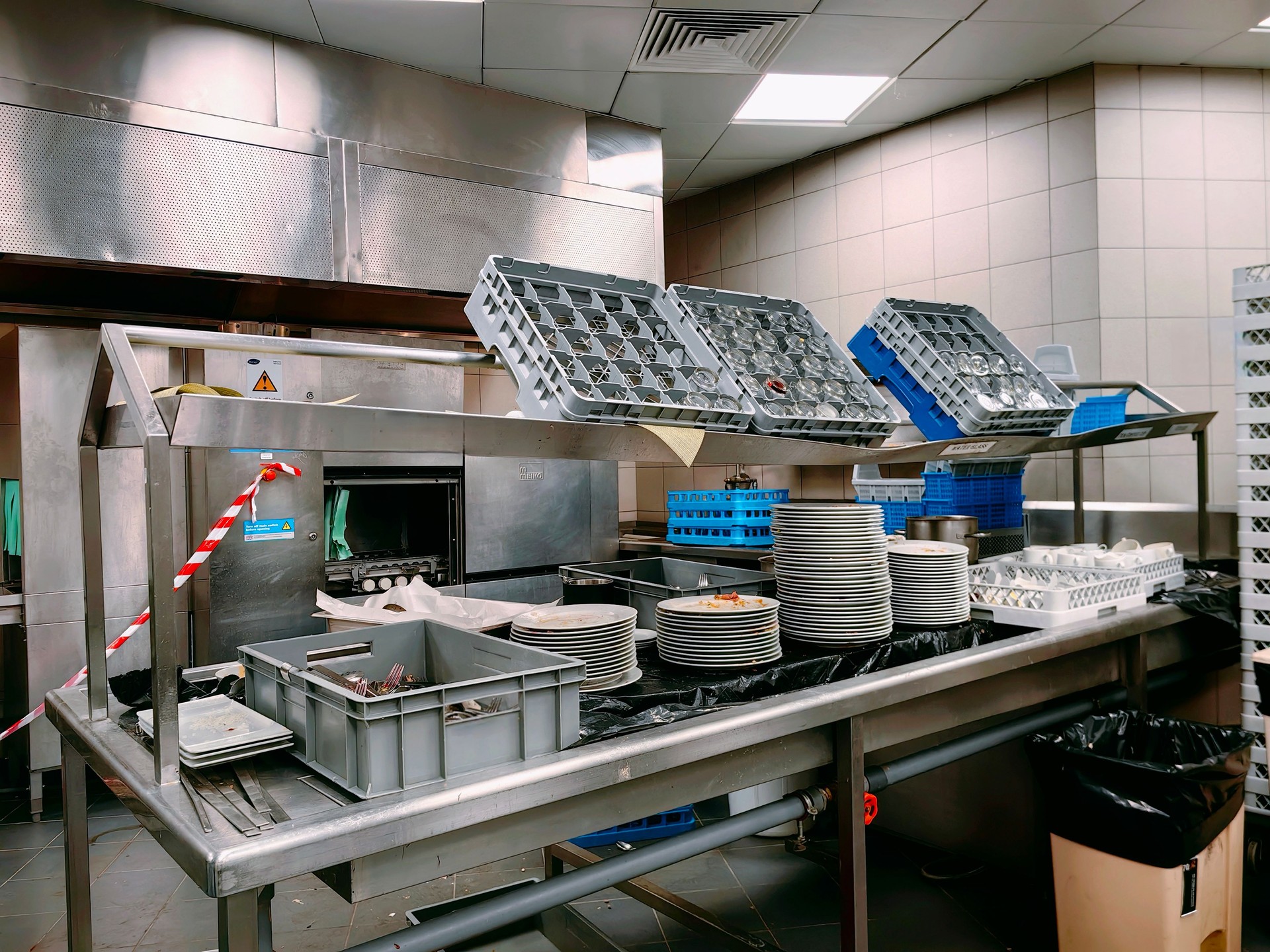 The steward area looks full of dirty glasses and plates near the dishwasher machine.